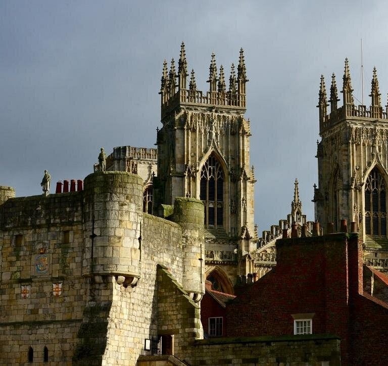 The historic stone towers of York Minster cathedral rise behind a medieval city wall under a grey sky.