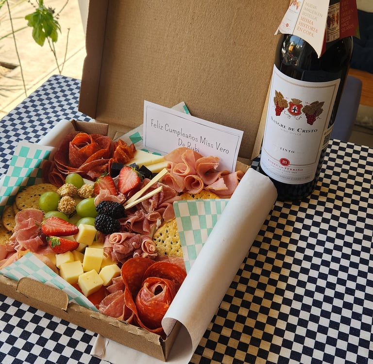 Gourmet charcuterie board gift box with cured meats, cheese, and fruit next to a bottle of red wine.