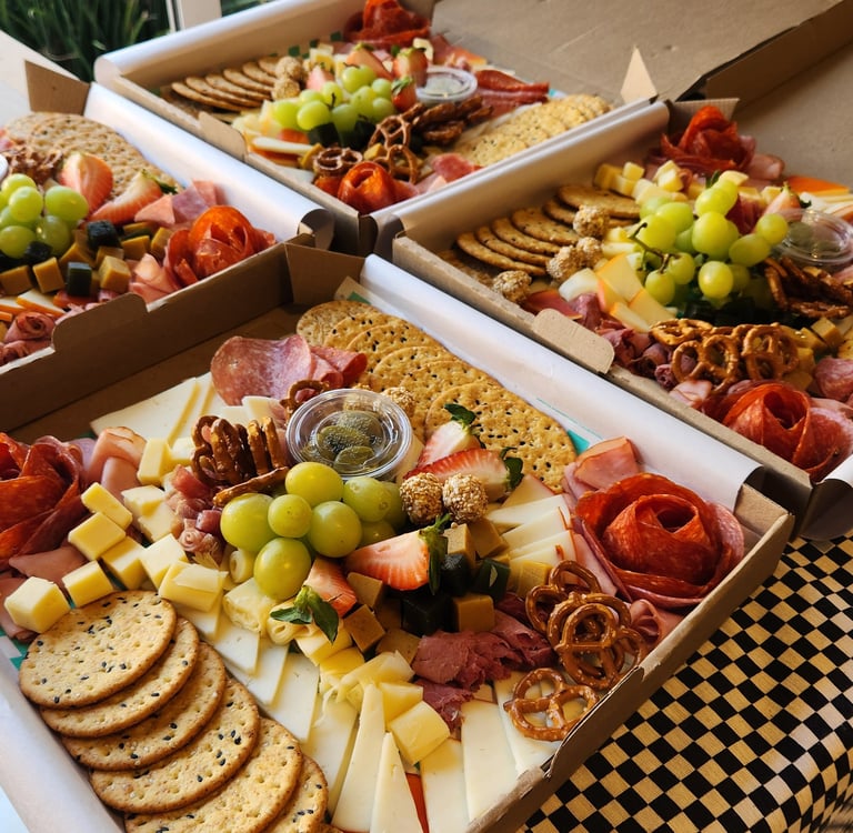 Gourmet charcuterie boxes with artisanal cheeses, salami roses, crackers, grapes, and pretzels.