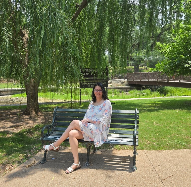 Angela sitting on a bench in the park under a tree.