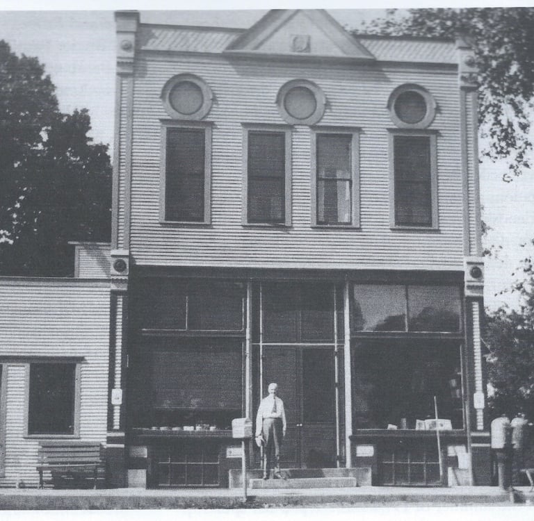 a two story white building with a man standing in front of it