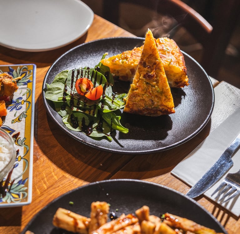 A plate of Spanish tortilla omelette slices served with balsamic glazed spinach and cherry tomatoes.