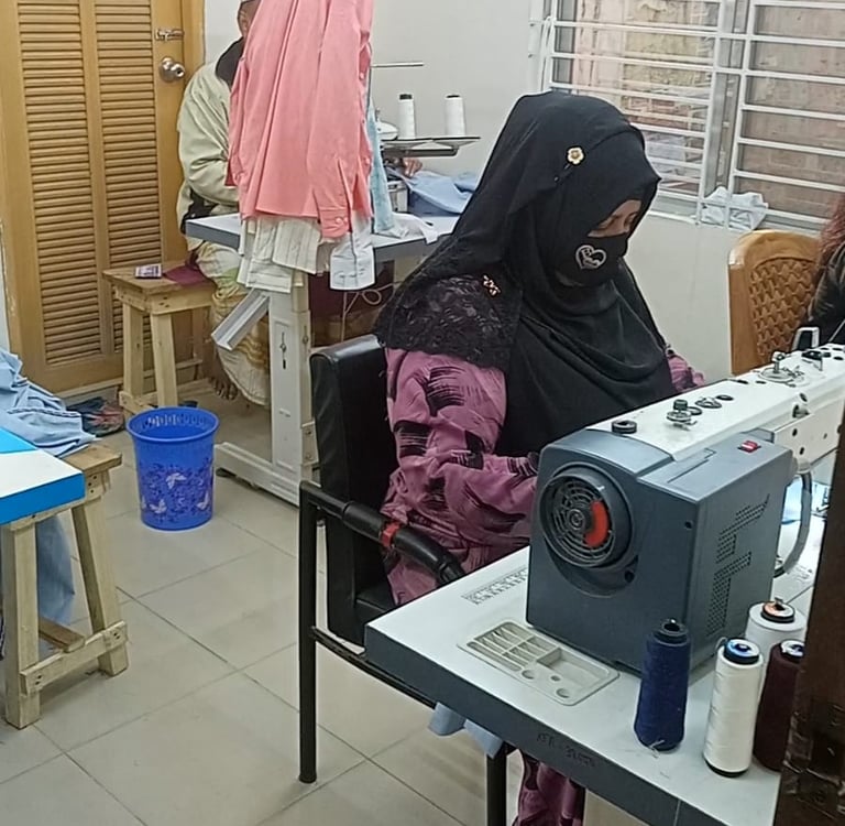 A seamstress wearing a black niqab operates an industrial sewing machine in a professional garment workshop.