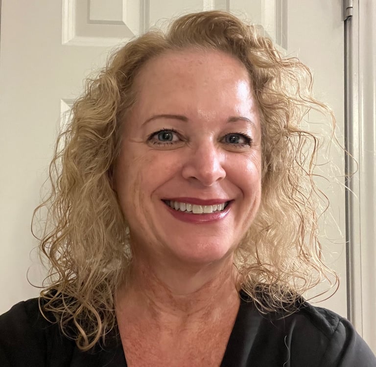 Smiling blonde woman with curly hair wearing a black shirt in front of a white door.
