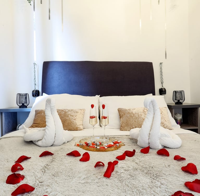 The photo shows a bed decorated for a honeymoon special in the BDSM Love Apartment with champagne and rose petals.
