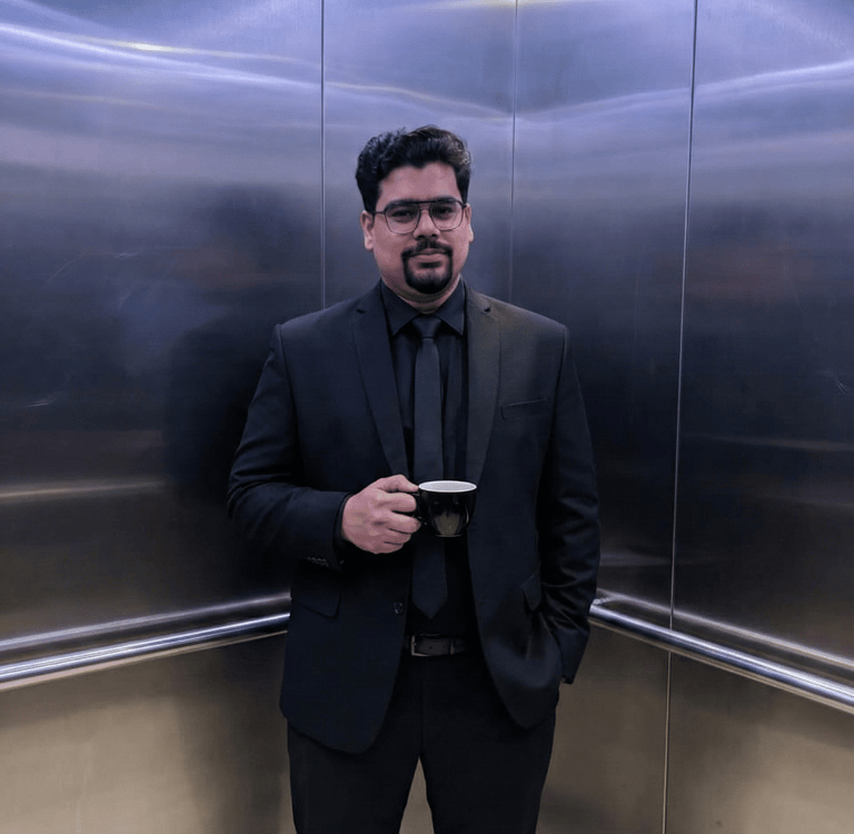 Professional businessman in a black suit holding a coffee mug inside a modern elevator.