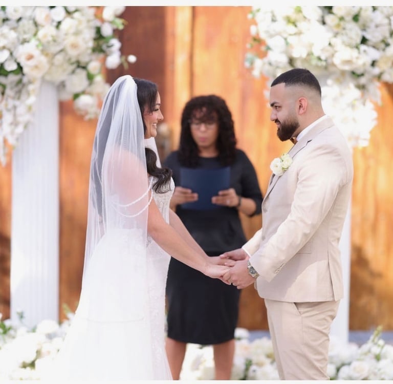 Bride and groom holding hands during an outdoor wedding ceremony with white floral arrangements.