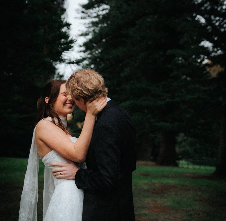 Smiling bride and groom embrace during a moody outdoor wedding photoshoot in a forest.