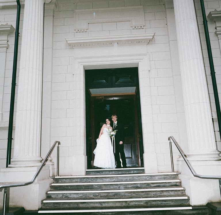 A bride and groom posing at the entrance of a historic building with large white columns.