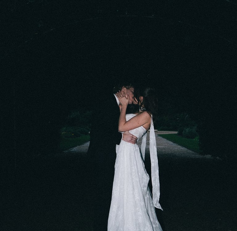 A bride and groom sharing a romantic kiss at a dark night wedding ceremony outdoors.