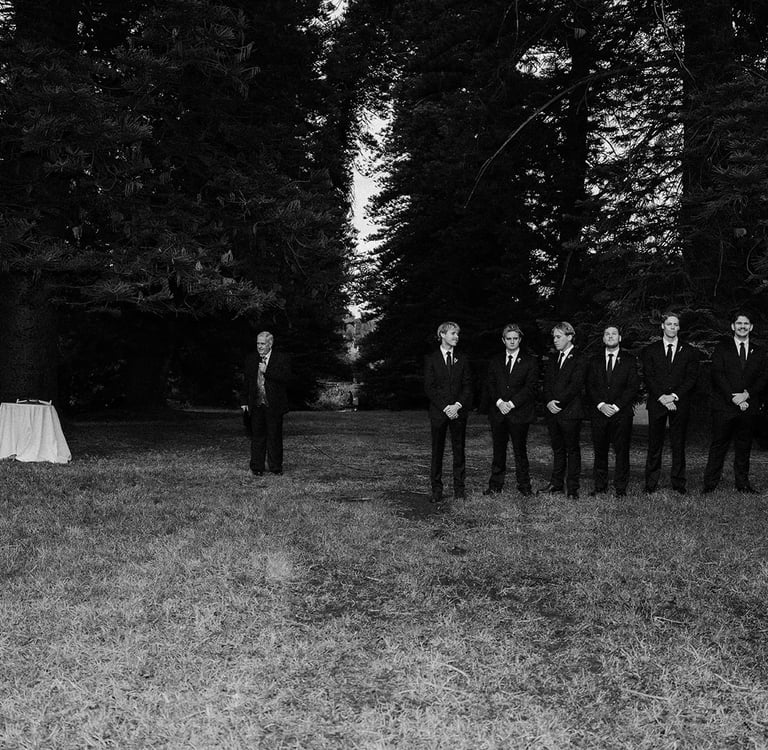 Groom and groomsmen in black suits standing in a forest for a woodland wedding ceremony.