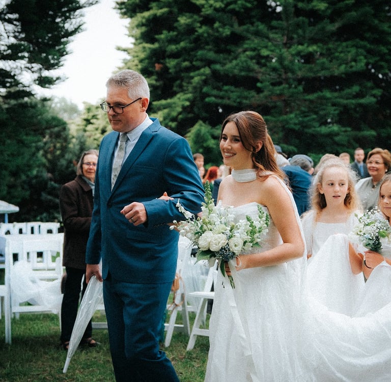 Bride arriving at the ceremony beneath the pine trees at Adelaide Botanic Garden