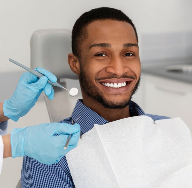 A smiling man as a dentist holds instruments nearby.