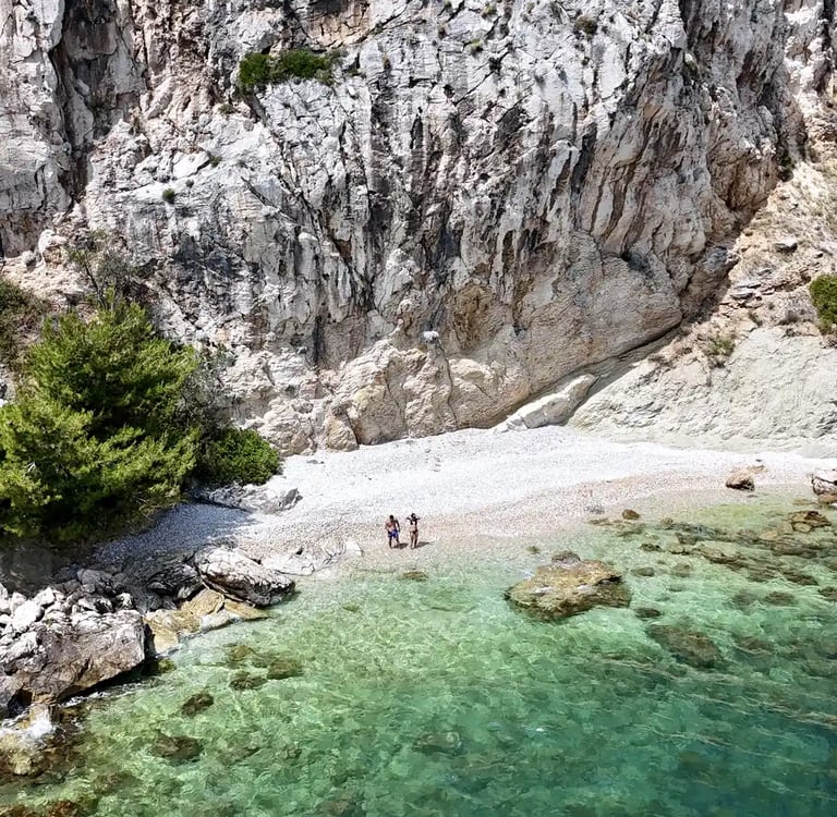 Aerial panoramic view of a hidden beach, a couple and dramatic cliffs on Ciovo during a private boat tour from Split, Croatia
