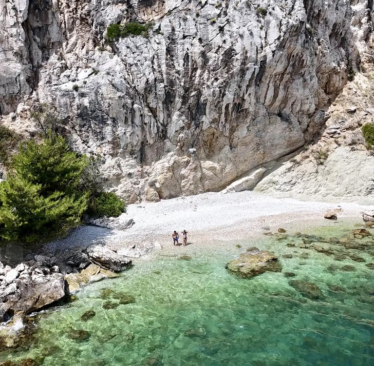 Aerial panoramic view of a hidden beach, a couple and dramatic cliffs on Ciovo during a private boat tour from Split, Croatia