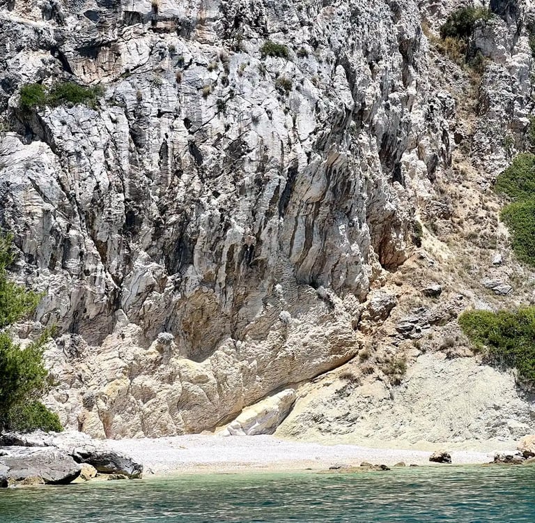 Sea level view of the hidden beach under cliffs on Ciovo Island, seen on a private boat tour off the coast of Split, Croatia.