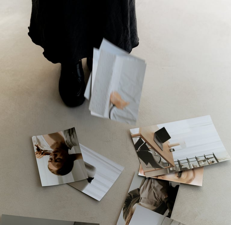 A person in a black midi-skirt dropping lifestyle photos and paperwork onto a minimalist floor.
