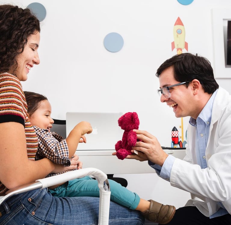 Un pediatra comparte una sonrisa y juega con un osito de peluche durante un chequeo médico.