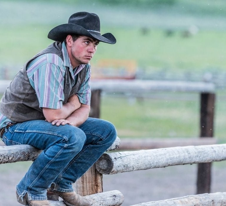 cowboy sitting on wood fence