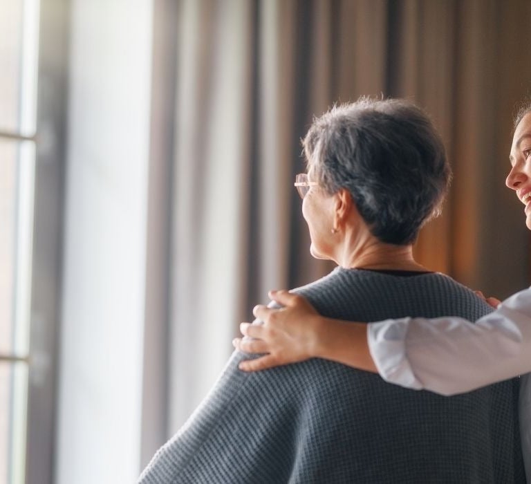 elderly woman looking out window next to nurse