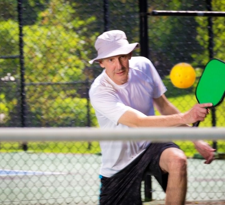 senior man with hat on playing pickleball