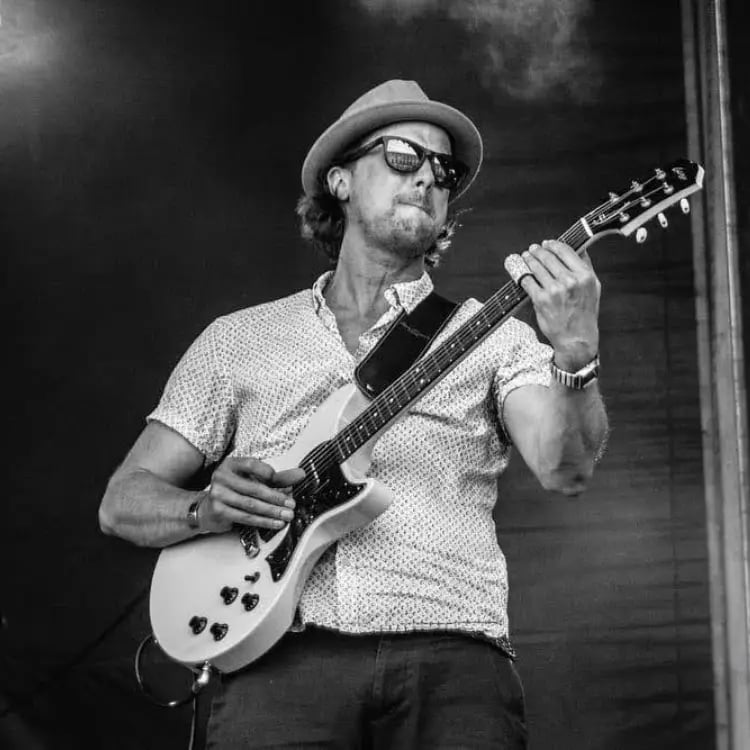 Lead guitarist of Mosaic performing a high-energy country-rock solo at a festival-style wedding