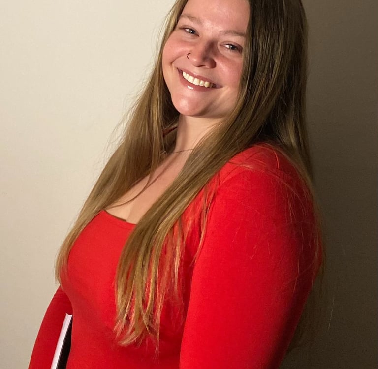 A smiling young woman with long blonde hair wearing a vibrant red top posing for a professional headshot.