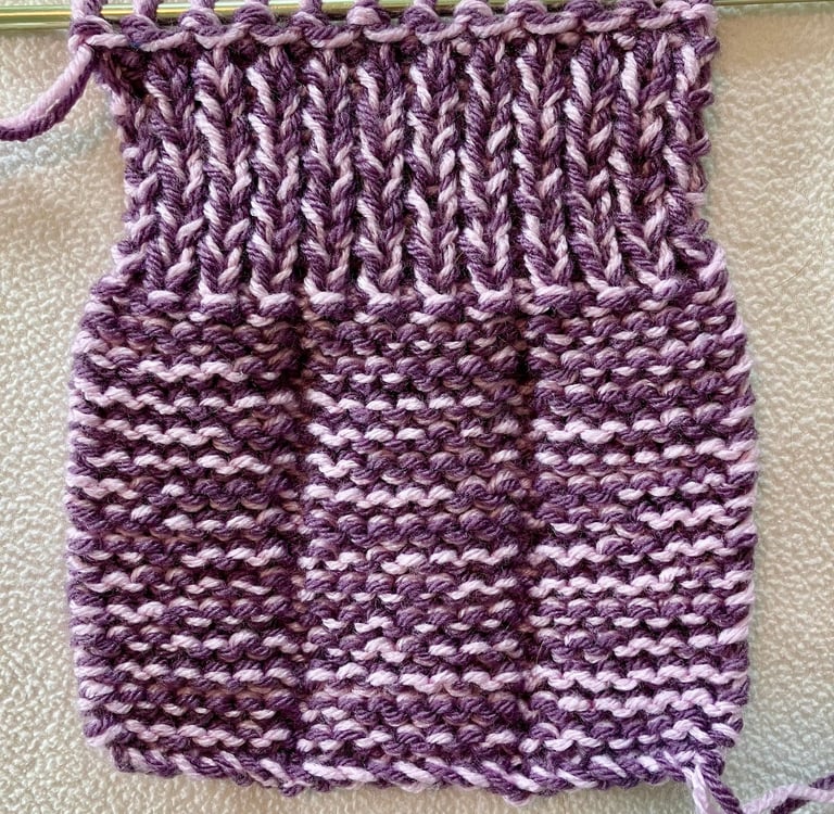 Flat knitted purple slipper on knitting needle, wrong side showing