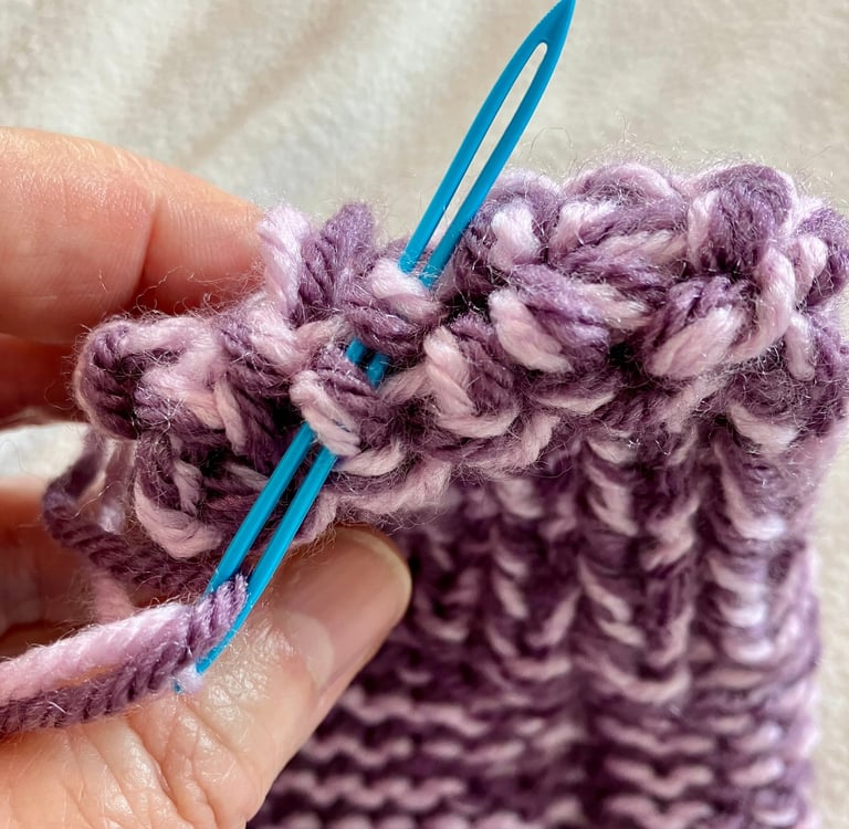 Close-up of yarn needle sewing together end of knitted toe of purple slipper
