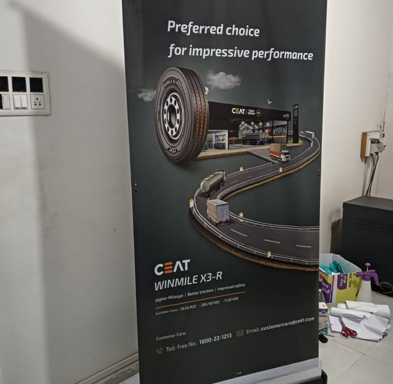 CEAT Winmile X3-R truck tire advertisement on a vertical banner stand in an indoor office setting.
