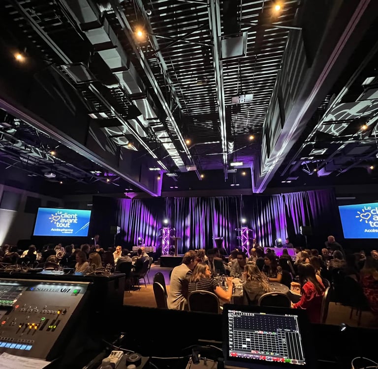 Corporate event gala with guests seated at tables facing a purple stage with AV mixing consoles in the foreground.