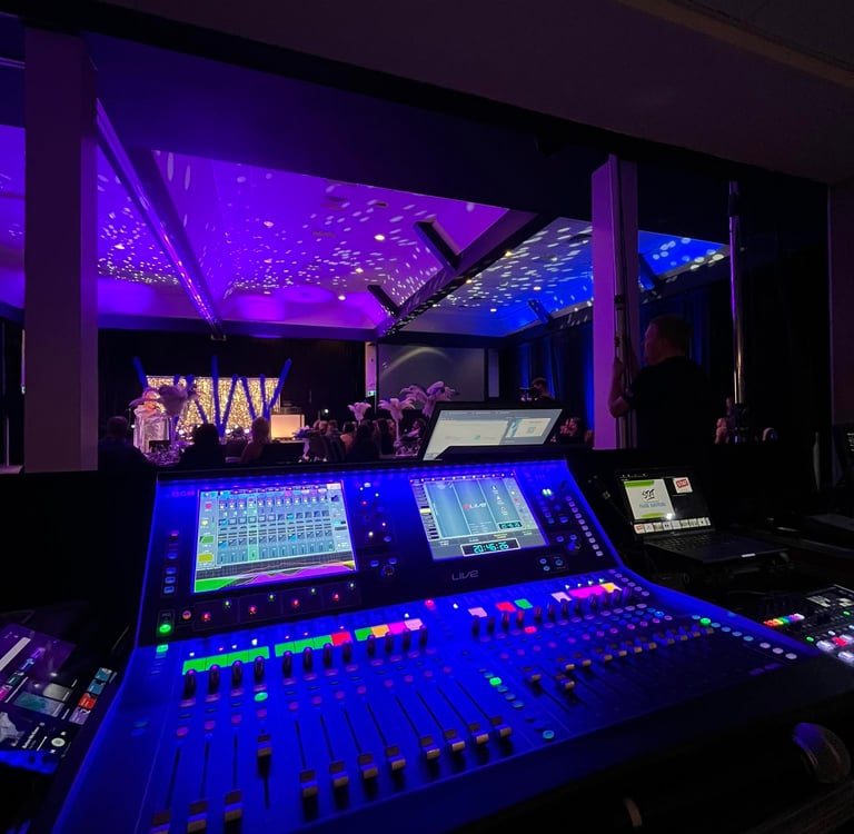 Professional digital audio mixing console at a live event with purple stage lighting.