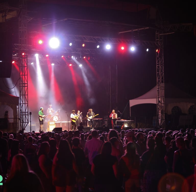 Live band performing on a lit outdoor stage at VictoFest for a large crowd at night.