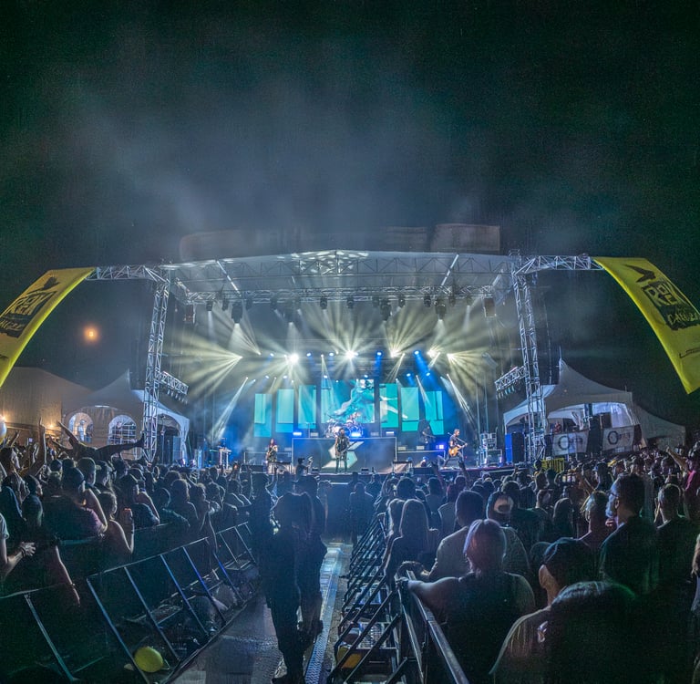 Live rock band performing on a large outdoor concert stage with professional lighting and a crowd.