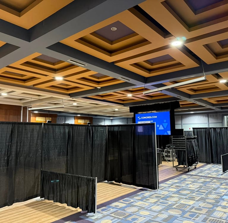 Empty conference room with black pipe and drape partitions, patterned carpet, and a modern coffered ceiling.