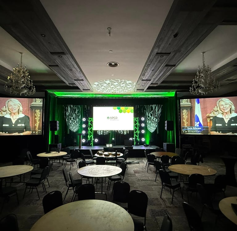 Professional conference room setup with green stage lighting, round banquet tables, and large projection screens.