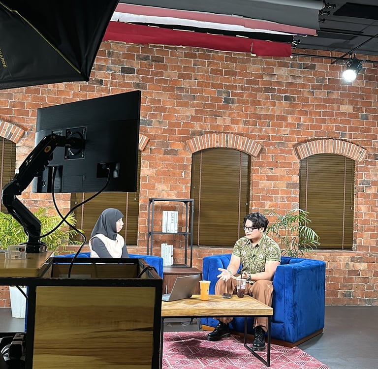 Professional podcast studio set with guests on blue velvet sofas against a brick wall background.