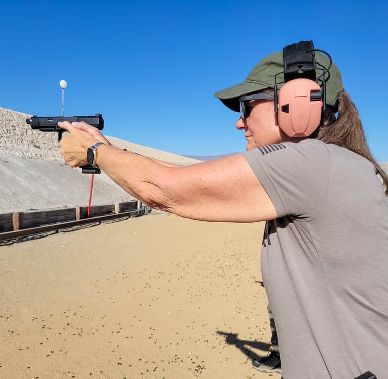 A woman at an outdoor firing range practicing target shooting with a black semi-automatic handgun.