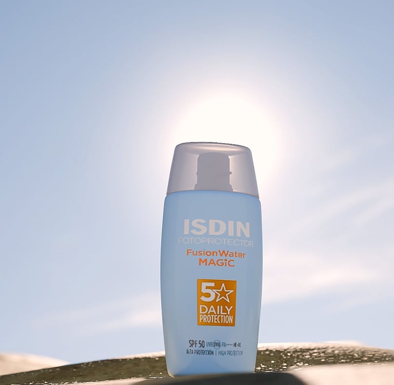 Bote de crema de sol de ISDIN en la arena y el sol detrás.