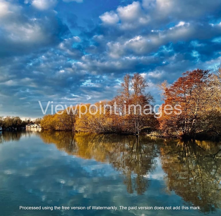 Tranquil river landscape with autumn trees reflecting in calm water under a dramatic blue sky.