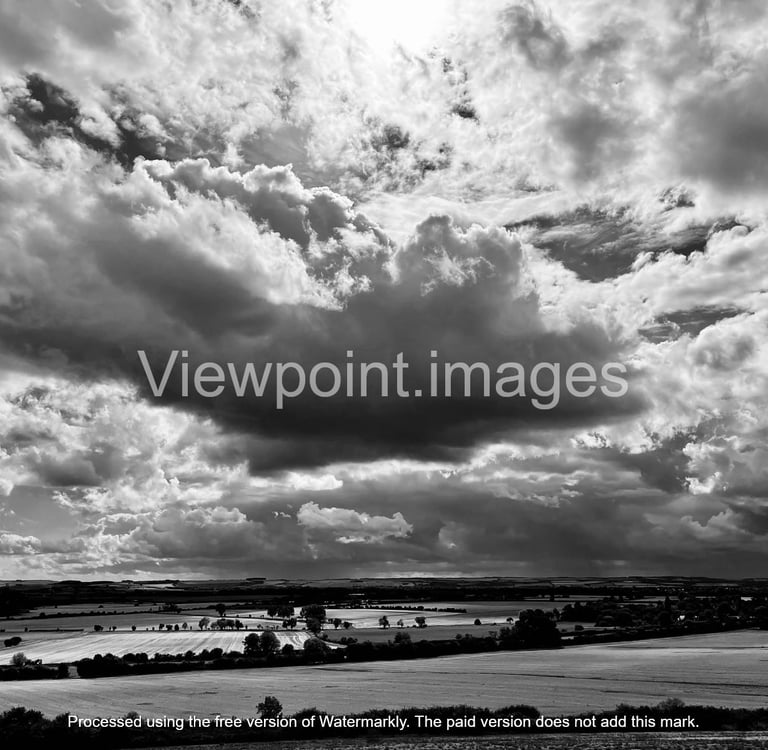 Dramatic black and white landscape of storm clouds over rural farmland and fields.