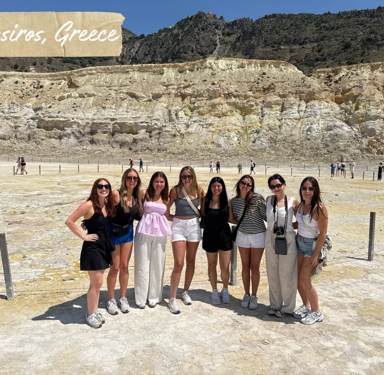A group of women travelers posing inside the volcanic crater of Nisyros, Greece, with rocky terrain behind.
