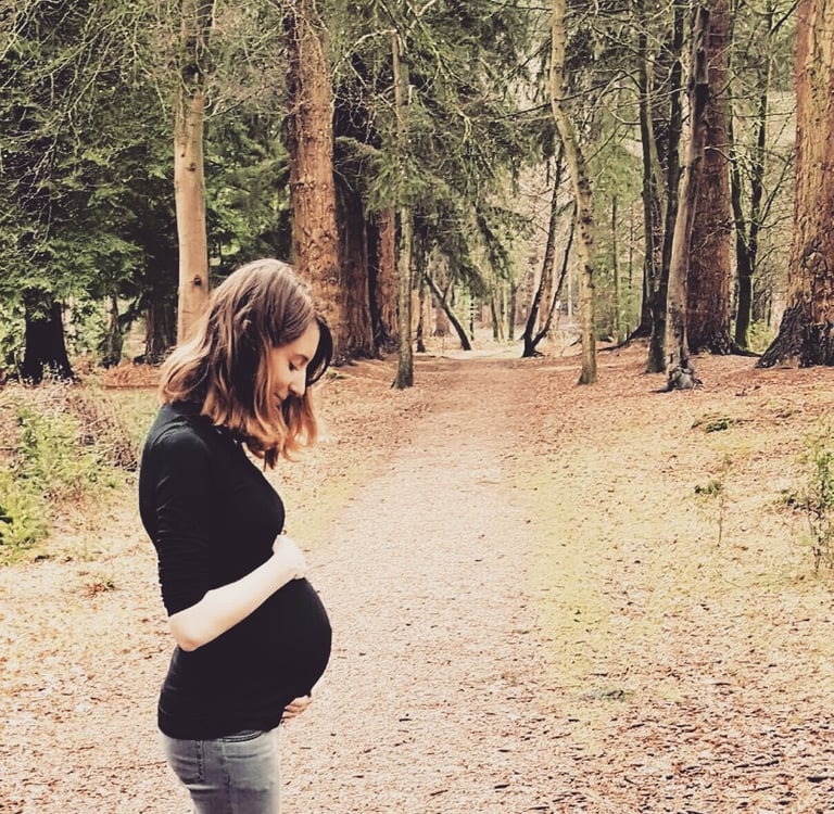 pregnant woman standing in a forest holding her bump