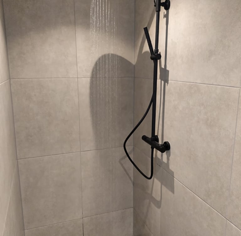 Zwarte douche in sobere badkamer met grote tegels.