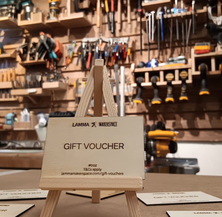 Wooden gift voucher on a miniature easel in a fully equipped Lamma Makerspace workshop.