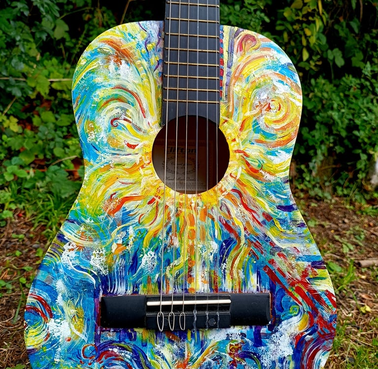 peinture sur guitare aux couleurs vives, avec un soleil autour de la rosace et des formes abstraites