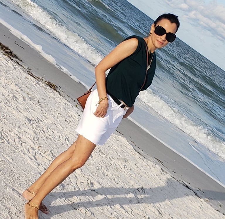 a woman in white shorts and sunglasses on a beach