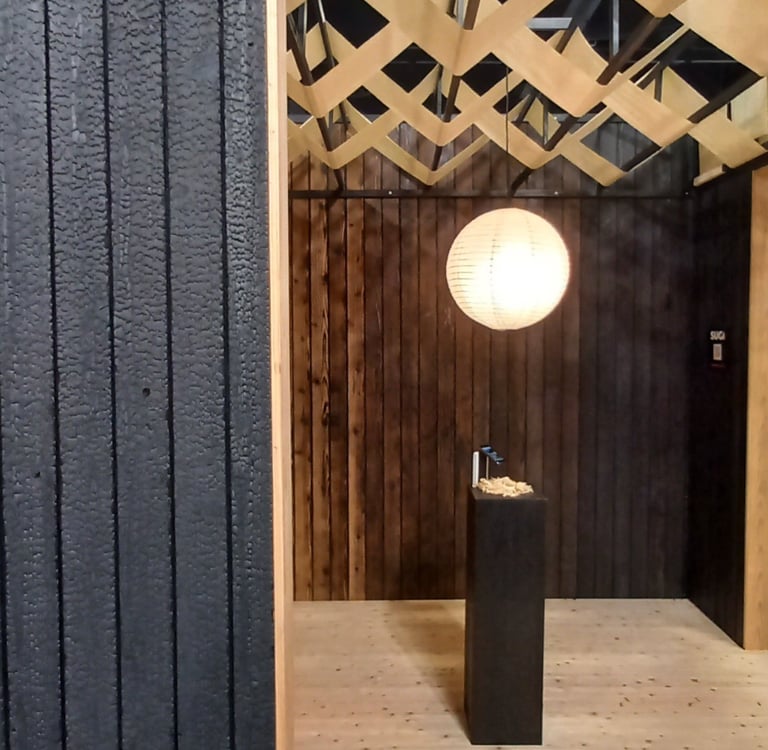 Modern interior with Shou Sugi Ban charred wood walls, paper lantern, and decorative wood ceiling installation.