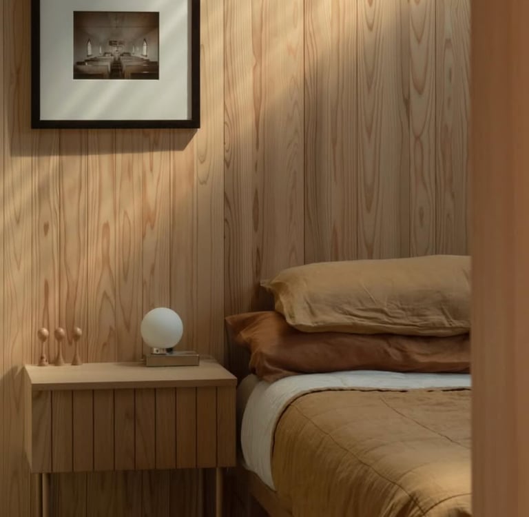 Minimalist bedroom with light wood paneling, a wooden nightstand, and linen bedding in warm earthy tones.