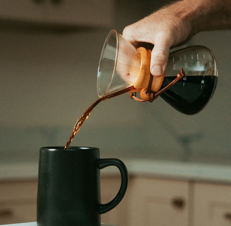 Mano sirviendo café filtrado en una taza negra usando chemex, mostrando métodos de preparación artes